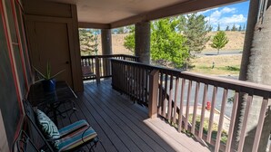 A covered porch with a wooden deck, a seating area with striped cushions, and a view of a grassy landscape with trees and a road. - In-town Durango Getaway | Pool | Hot Tub (Durango)