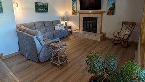 A living room with a grey sofa, a wooden coffee table, a fireplace, a television mounted on the wall, and a rocking chair. - In-town Durango Getaway | Pool | Hot Tub (Durango)