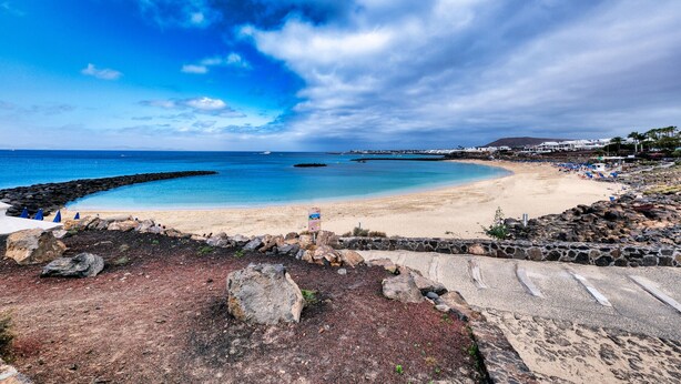 Una playa con cielo despejado, primer plano rocoso y una montaña distante.