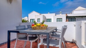 Una terraza con una mesa, sillas y una cesta de frutas.