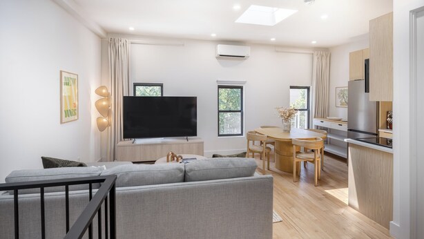Un salon moderne avec un canapé gris, un téléviseur à écran plat et un coin repas comprenant une table et des chaises en bois.