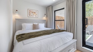 Une chambre à coucher avec un lit, une fenêtre avec des rideaux, un luminaire fixé au mur et un tableau encadré.