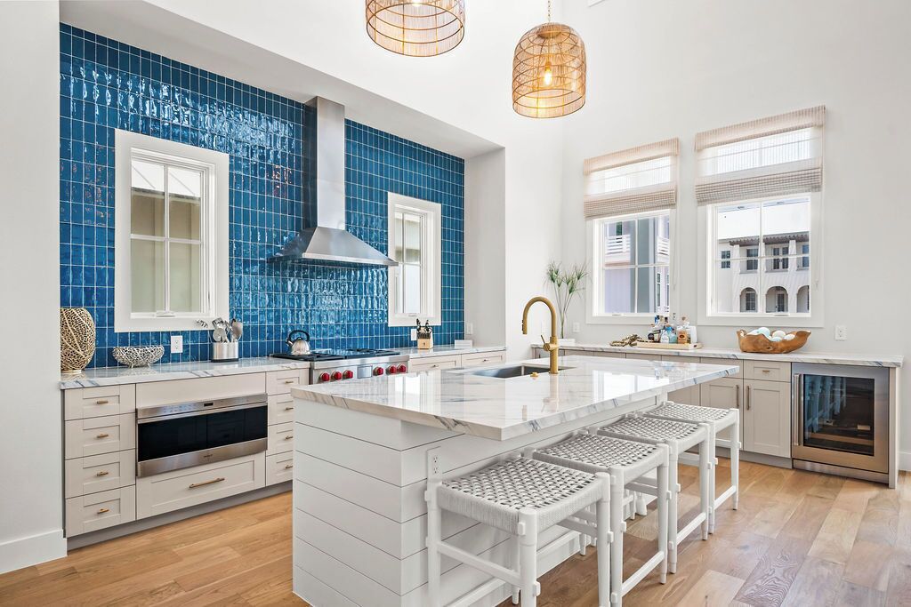 A modern kitchen with a blue tiled backsplash, white cabinetry, a central island with bar stools, and pendant lighting.