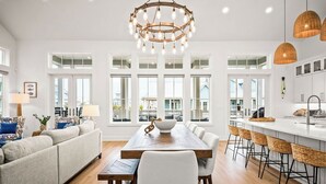 A spacious living room with a large wooden dining table, white sofas, and a modern chandelier. - Pelican Place 108 RET (Port Aransas)