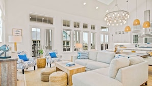 A spacious living room with a large sectional sofa, a coffee table, and a dining area with a kitchen in the background. - Pelican Place 108 RET (Port Aransas)