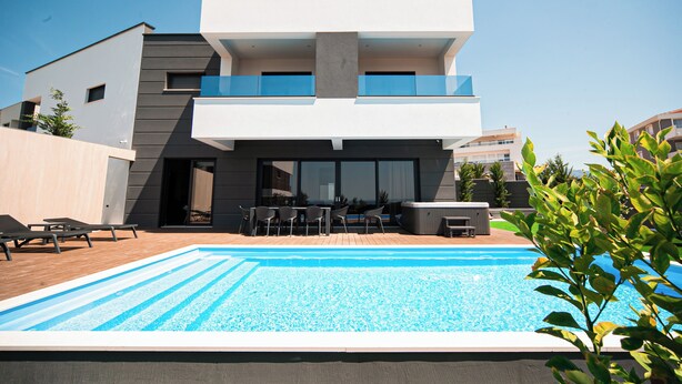 Une maison moderne à deux étages, dotée d’une piscine, d’un espace salon extérieur et d’un balcon.