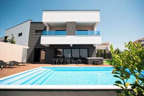 Una casa moderna de dos pisos con piscina, mobiliario exterior y balcón.