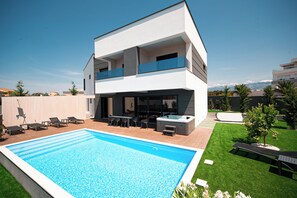 A modern two-story house with a swimming pool, outdoor seating, and a hot tub.