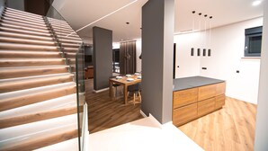 Un intérieur moderne avec un escalier en bois, un coin repas et une cuisine dotée d’un plan de travail en bois.
