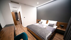Une chambre d’hôtel moderne avec un plancher en bois, un lit avec une literie grise, une chaise bleue et un bureau.