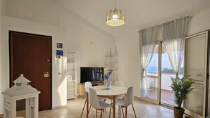 A modern living room with a dining area, a large window with curtains, and a view of the outdoors. - Apartment with sea-view terrace for breathtaking sunsets. (Nebida)