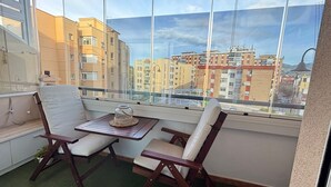 Un balcón con dos sillas y una mesita, con vistas a un paisaje urbano con edificios de varios pisos.