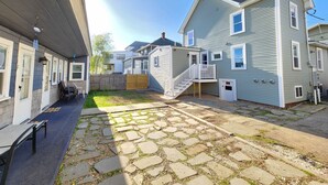 A residential area with a paved courtyard, a wooden fence, and a two-story house with a balcony.