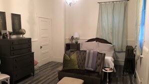 Ein gemütliches Wohnzimmer mit einem dunklen Sofa, einem kleinen Holzschemel, einer Kommode und einer Lampe.