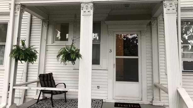 Eine weiße Veranda mit einem Stuhl und zwei hängenden Pflanzen.