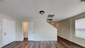Een ruime kamer met houten vloeren, witte wanden en een deur naar een andere kamer.
