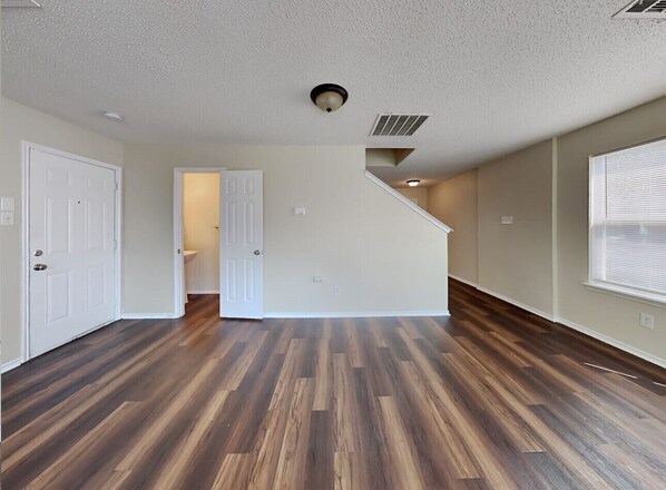 A spacious room with hardwood flooring, white walls, and a door leading to another room.