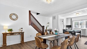 A dining area with a wooden table, six chairs, a chandelier, and a staircase. - Renovo Escape: Game Room + Spa Bath + Views (Renovo)