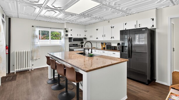 A modern kitchen with white cabinetry, a central island with bar stools, a black refrigerator, and a window with a view of greenery. - Renovo Escape: Game Room + Spa Bath + Views (Renovo)