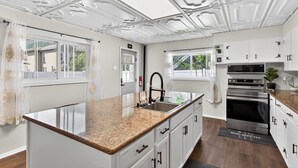 A modern kitchen with white cabinetry, a granite countertop, stainless steel appliances, and a decorative ceiling. - Renovo Escape: Game Room + Spa Bath + Views (Renovo)