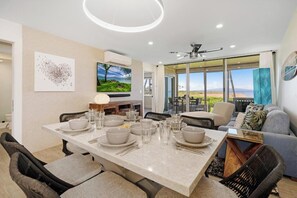 A modern dining area with a large table set for four, a sofa, and a TV mounted on the wall.