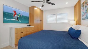 A bedroom with a bed, a ceiling fan, a TV on the wall, and a window with blinds.