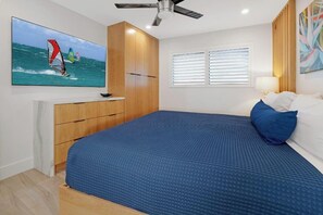 A bedroom with a bed, a ceiling fan, a TV on the wall, and a window with blinds.
