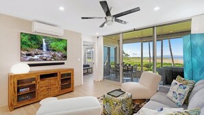 A modern living room with a flat-screen TV, a ceiling fan, and a large sliding glass door leading to an outdoor area.