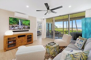 A modern living room with a flat-screen TV, a ceiling fan, and a large sliding glass door leading to an outdoor area.