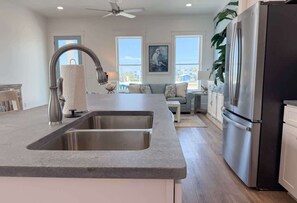 A modern kitchen with a double sink, stainless steel appliances, and a view of the outdoors. - A Serenity by the Sea St George Island Pool Home (Eastpoint)