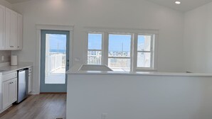 A modern kitchen with white cabinets, a dishwasher, and a large window overlooking a balcony.