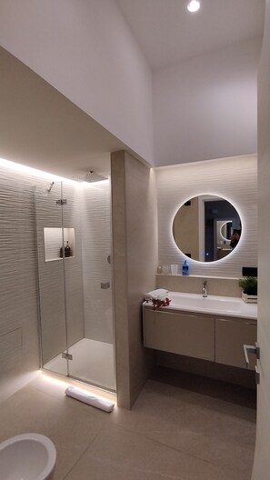 Un bagno moderno con doccia vetrata, uno specchio rotondo e un lavandino bianco.