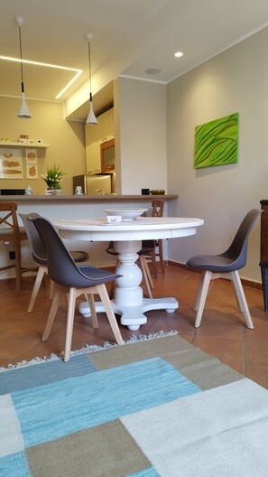 Un'area pranzo con un tavolo bianco, due sedie, un tappeto e una cucina sullo sfondo.