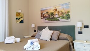 Une chambre d’hôtel avec un lit, deux tables de chevet, une lampe fixée au mur, un tableau et des serviettes soigneusement pliées.