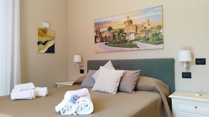 A hotel room with a bed, two bedside tables, a wall-mounted lamp, a painting, and neatly folded towels. - EasyDoro Apartment - apartment in the center of Palermo  (Palermo)
