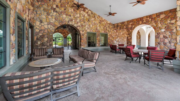 A spacious outdoor seating area with stone walls, multiple tables and chairs, and ceiling fans.