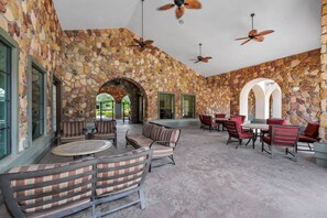 A spacious outdoor seating area with stone walls, multiple tables and chairs, and ceiling fans.