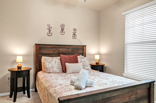 A neatly made bed with floral bedding, two bedside tables with lamps, and a window with blinds.