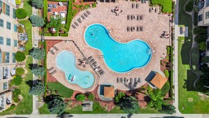 An aerial view of a hotel with a large central swimming pool, smaller pools, and outdoor seating areas.
