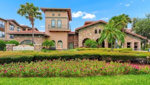 A multi-story hotel with a stone facade, a sign reading "Bella Riazza," and a well-maintained garden with pink flowers.