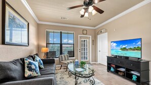 A living room with a dark-colored sofa, a glass coffee table, a television, and a ceiling fan.