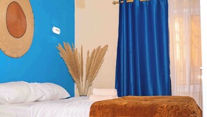 Een slaapkamer met een bed, een blauw gordijn, een hoed bevestigd aan de muur en pampa in een vaas.