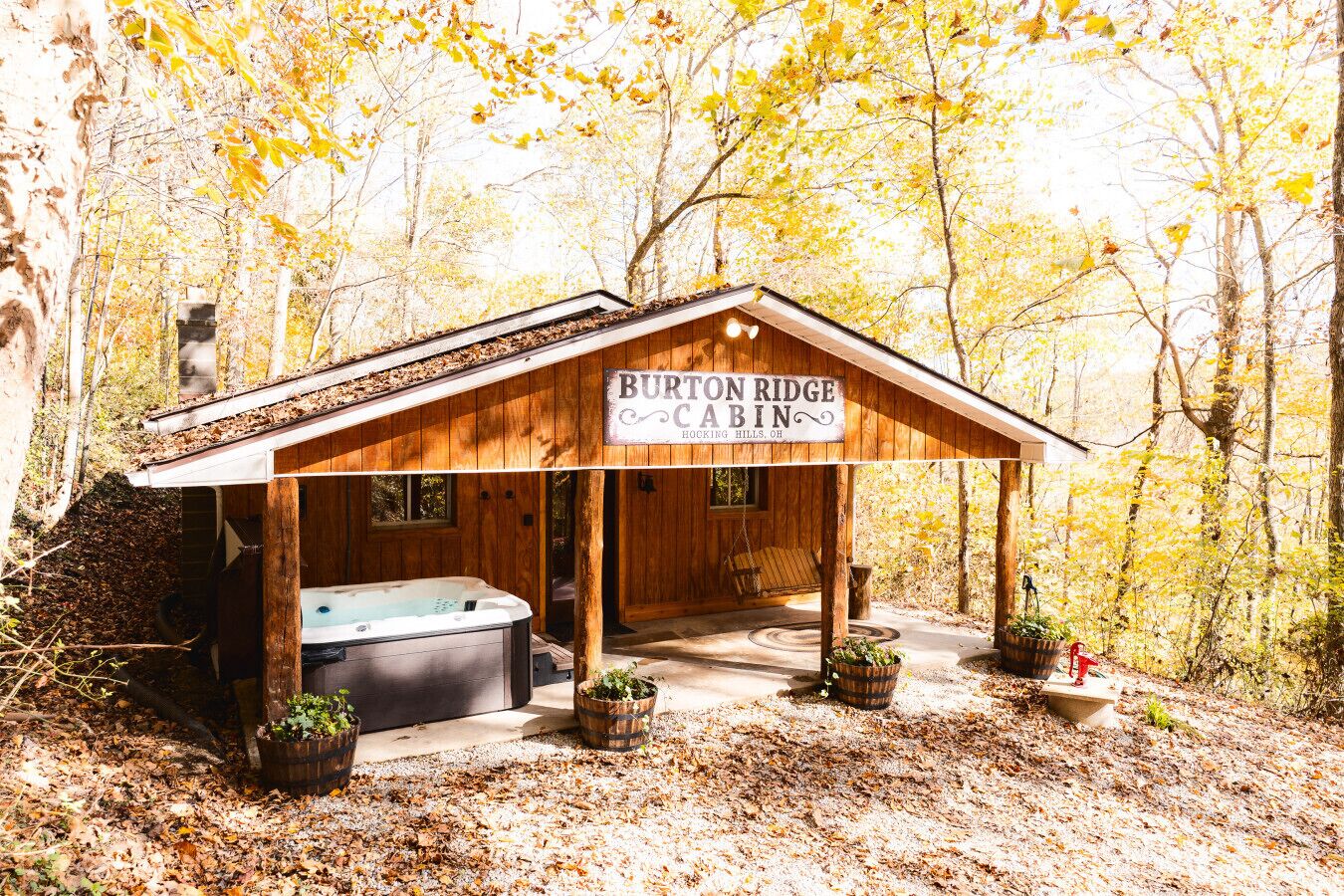 A cabin named "Burton Ridge Cabin" with a hot tub, wooden exterior, and surrounded by autumn trees.