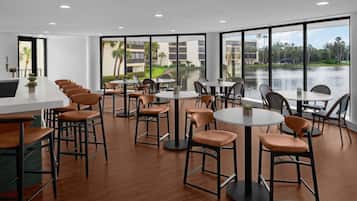 A modern indoor dining area with multiple tables and chairs, large windows offering a view of a body of water and buildings.