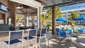 Un espace aménagé au bord de la piscine, avec des sièges de bar, des parasols et des chaises longues.