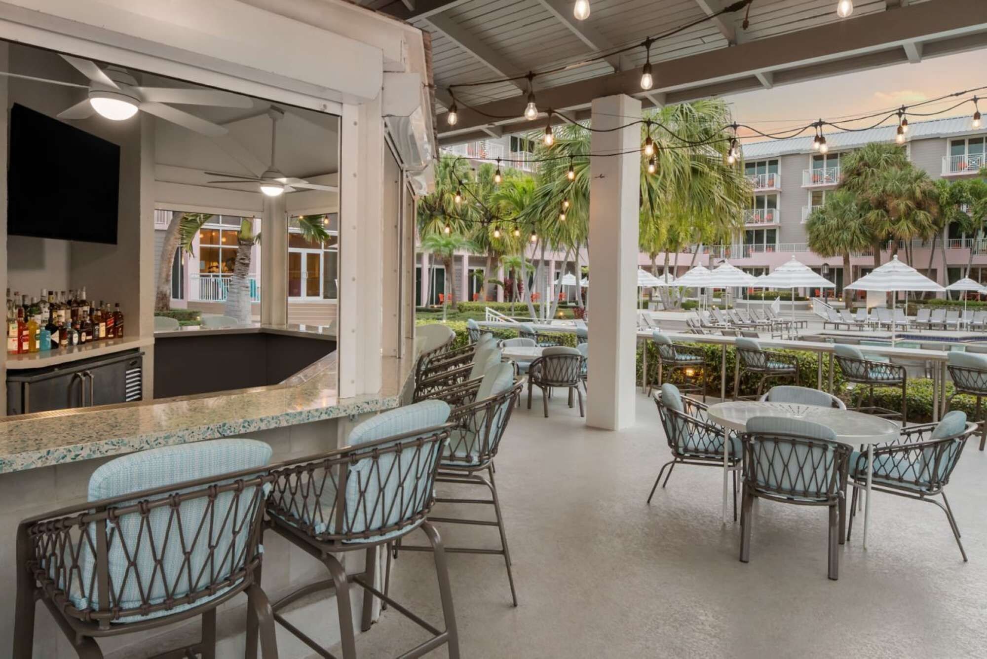 Zona de bar al aire libre con asientos, vista a la piscina y una barra repleta de botellas.