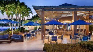 Un espace extérieur aménagé avec des parasols, des tables et des chaises, entouré de palmiers.