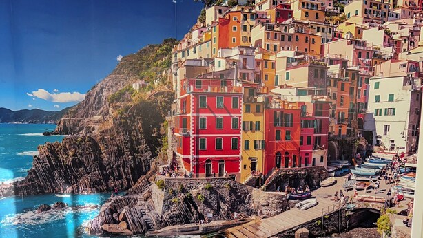 A hotel room with a bed, blue pillows, and a view of colorful buildings by the sea. - THE FIVE SAILS*****Water Front LUXURY HOUSE Genoa (Genova)