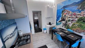 A modern kitchen with a gas stove, a sink, and a dining area with a table and chairs. There is a painting of a coastal town on the wall. - THE FIVE SAILS*****Water Front LUXURY HOUSE Genoa (Genova)