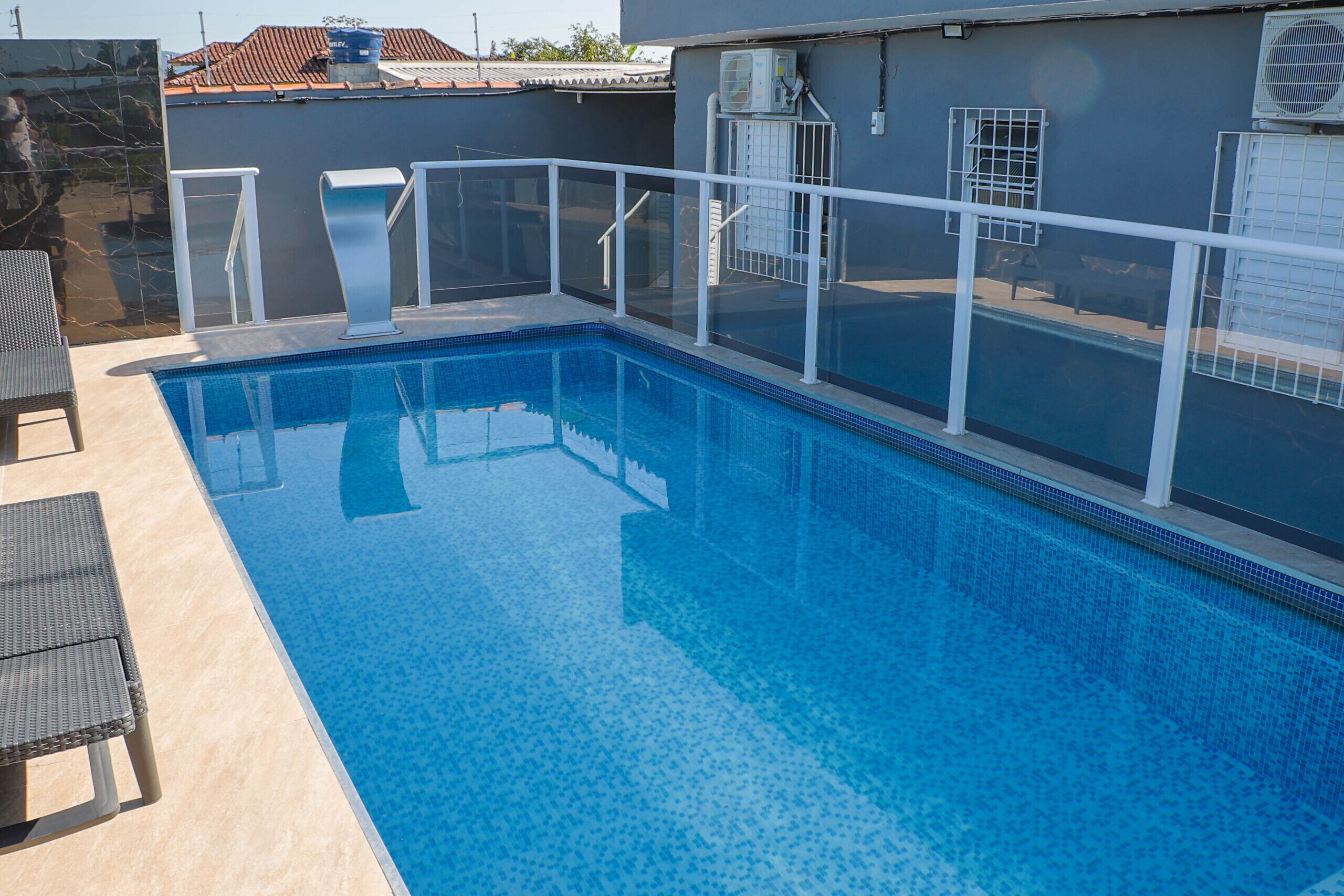 Uma piscina retangular com água azul cristalina, rodeada por uma cerca de segurança branca.